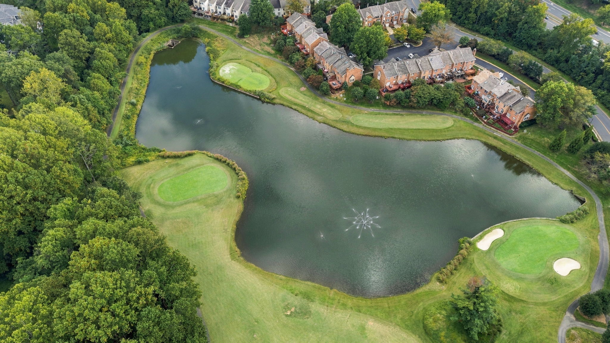 Penderbrook Golf Club — Aerial view of a pond and fountain with greens along the shore Aerial view of a pond and fountain with greens along the shore at Penderbrook Golf Club in Fairfax, Virginia